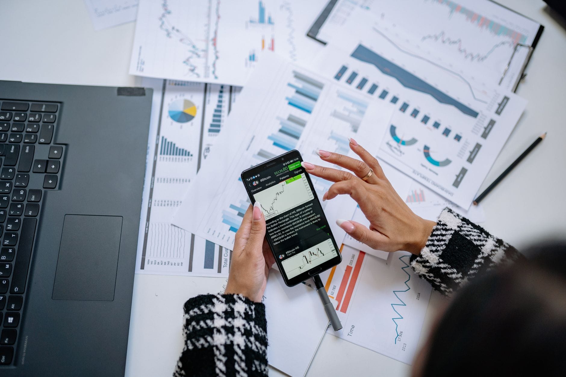 Bizneswoman analizuje wykresy finansowe na smartfonie przy laptopie