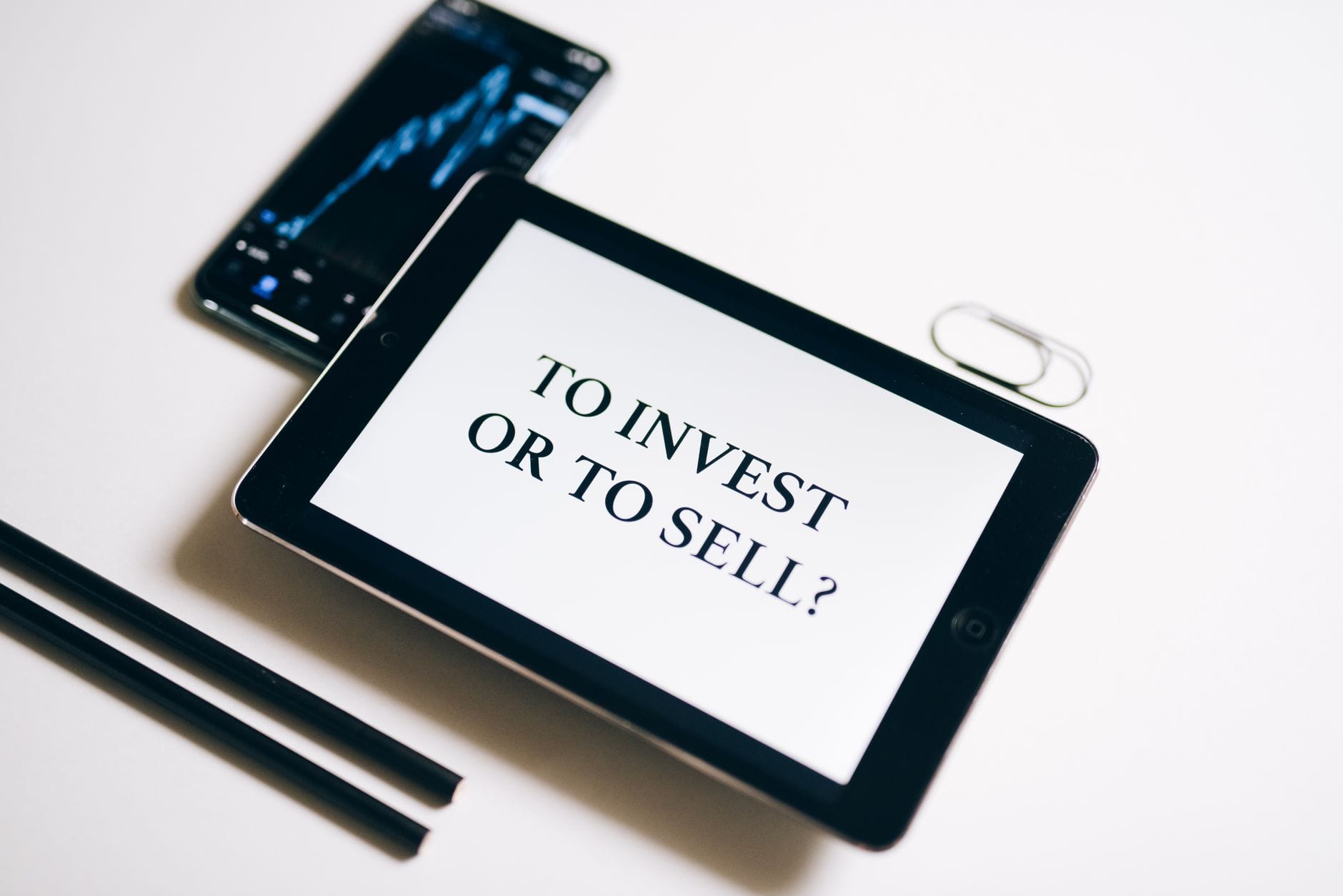 Tablet z napisem To Invest or To Sell na białym tle