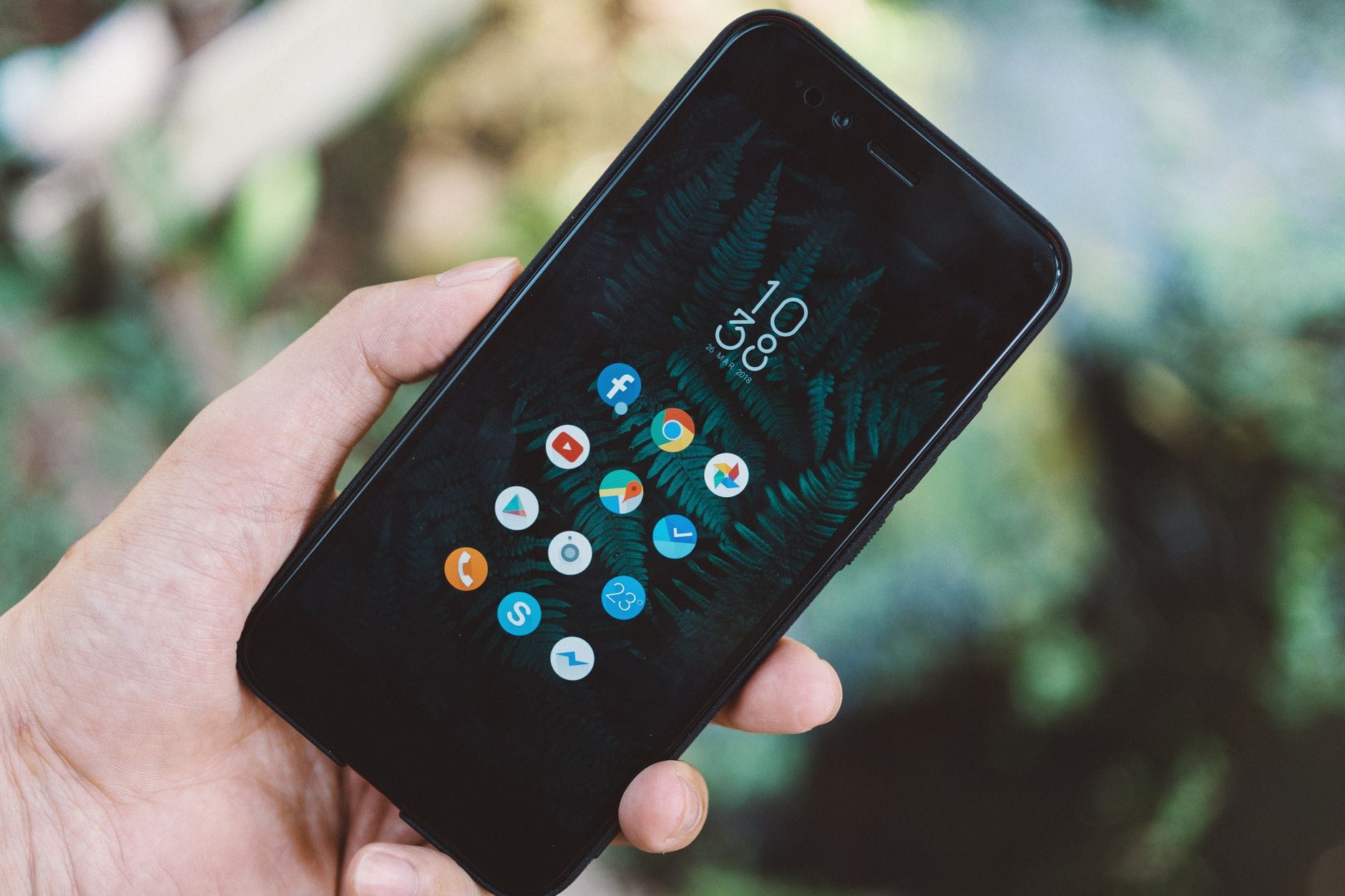 Dłoń trzymająca smartfon z ikonami aplikacji i tapetą z naturą