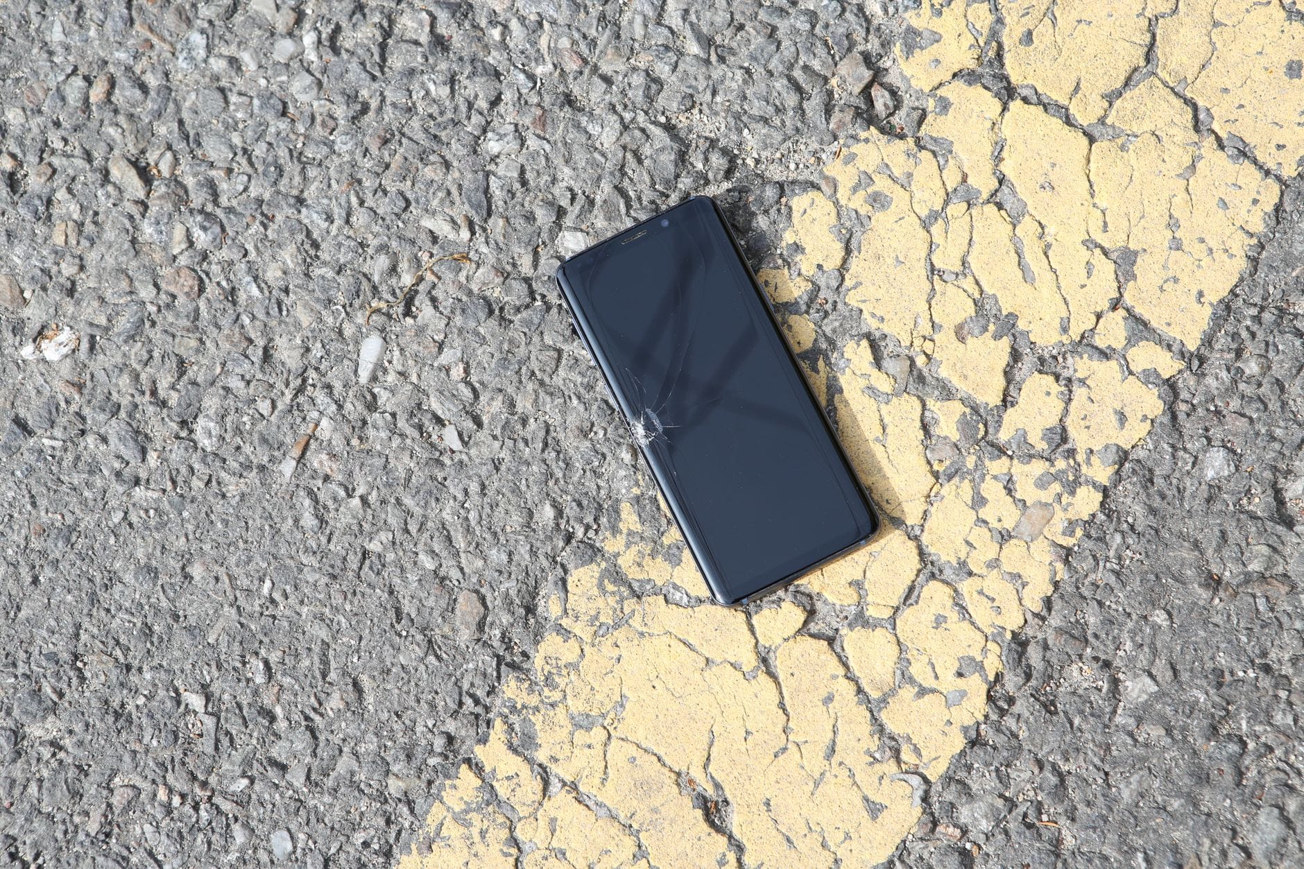 Pęknięty smartfon leżący na nasłonecznionym asfalcie