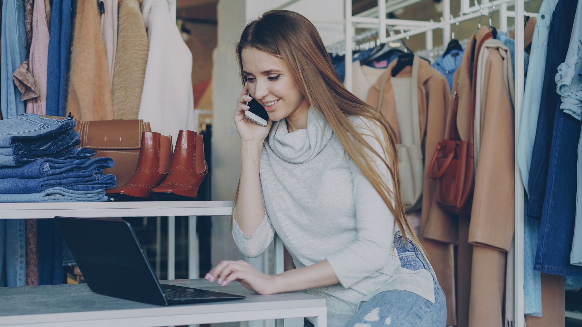 Sprzedawczyni w butiku zarządza ofertami na laptopie i smartfonie
