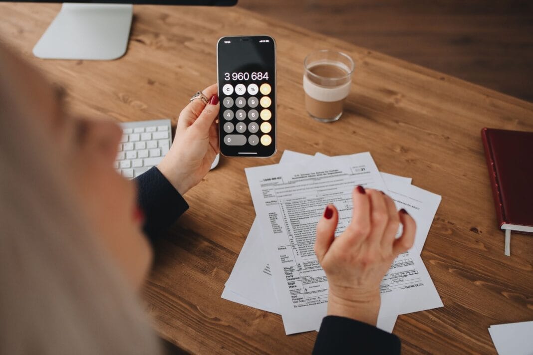 Kobieta obliczająca koszty na smartfonie przy biurku z dokumentami