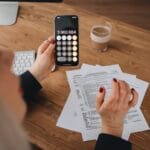 Kobieta obliczająca koszty na smartfonie przy biurku z dokumentami