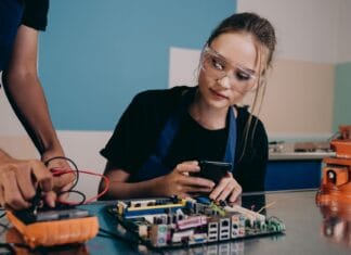 Techniczka sprawdza płytkę elektroniczną, korzystając ze smartfona